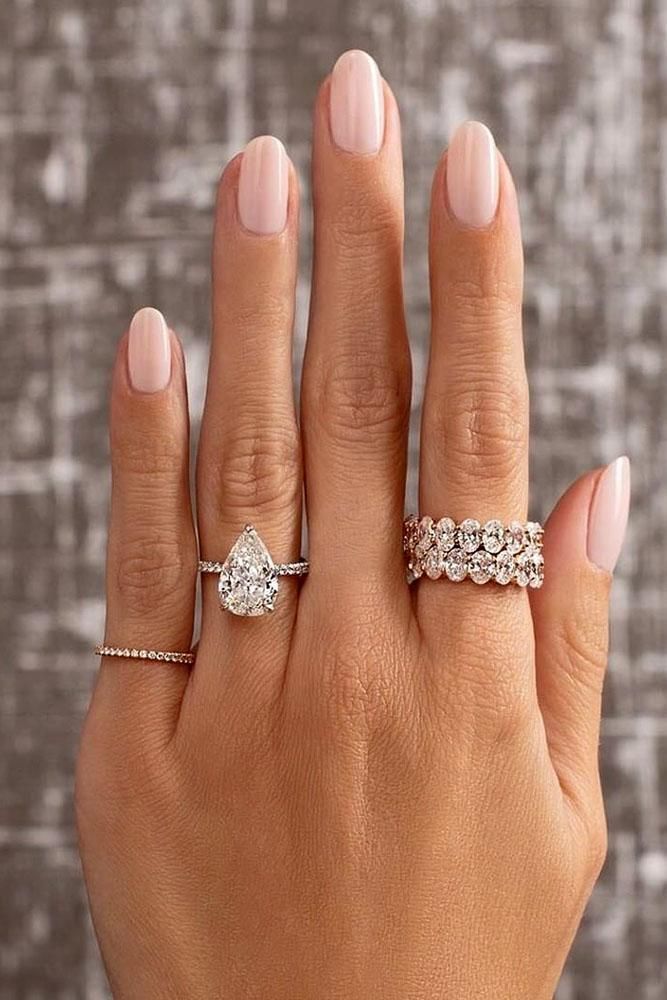 a woman's hand with two wedding rings on her left and the other hand holding an engagement ring