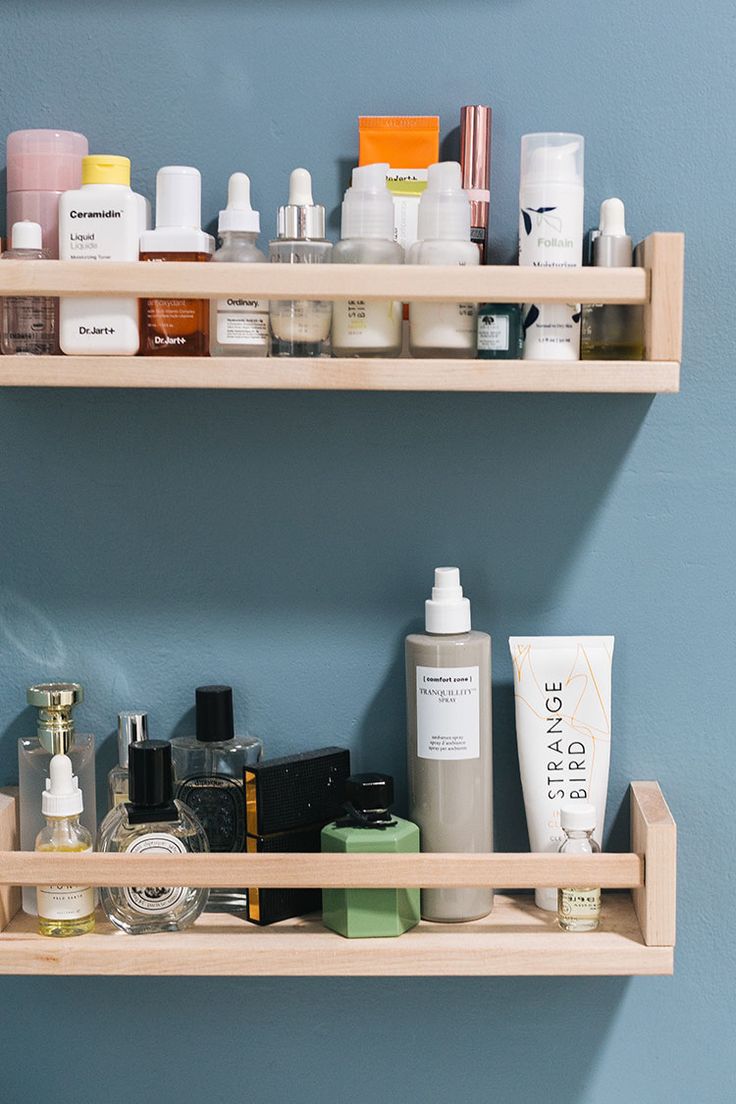 two wooden shelves filled with different types of skin care products and personal care items in front of a blue wall