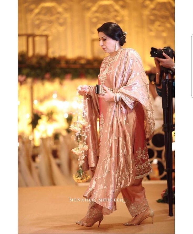 a woman in a pink and gold outfit walking down the aisle with her hand on her hip