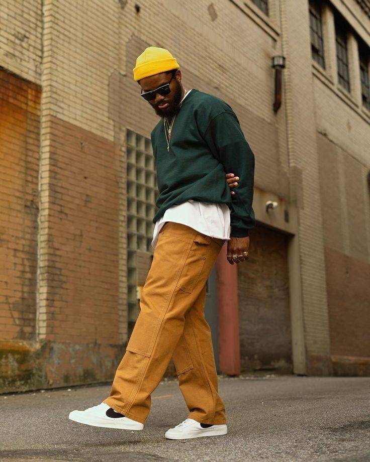 a man in green jacket and yellow hat walking on street next to brick building with white shoes