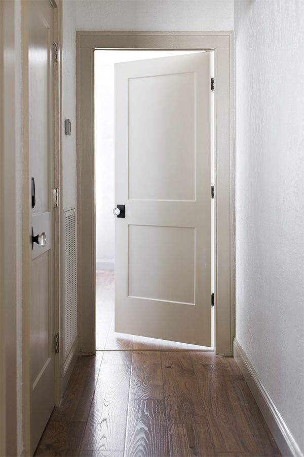 an empty hallway with a white door and wooden floors in front of the door is a light fixture