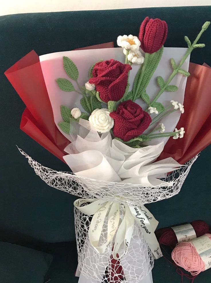 a bouquet of red and white flowers sitting on top of a table next to crochet doily