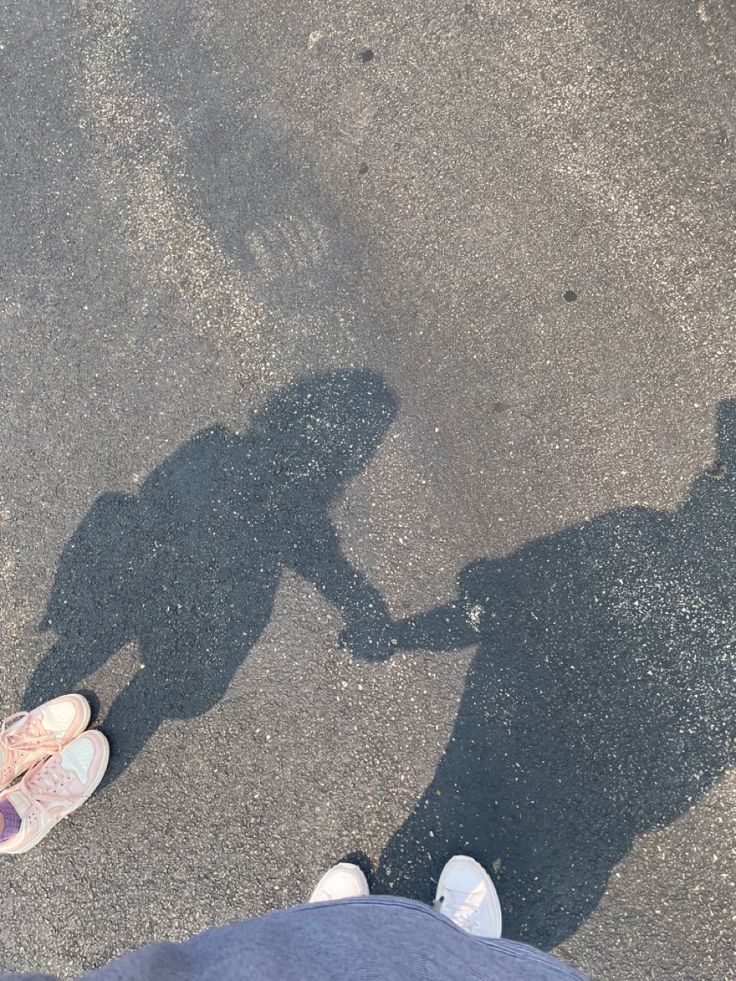 two people standing in the street with their shadows on the ground and one person holding his hand