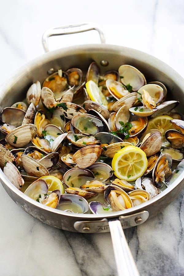 a pan filled with clams and lemon wedges on top of a marble counter