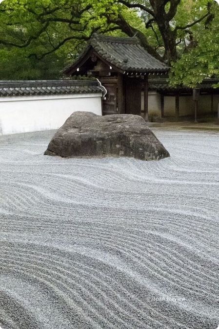 a large rock sitting on top of a gravel covered ground next to a building and trees