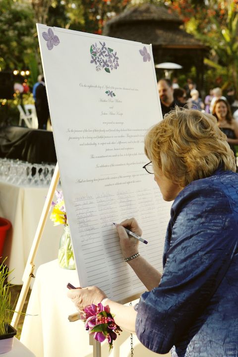 a woman writing on a piece of paper at an outdoor event with people in the background