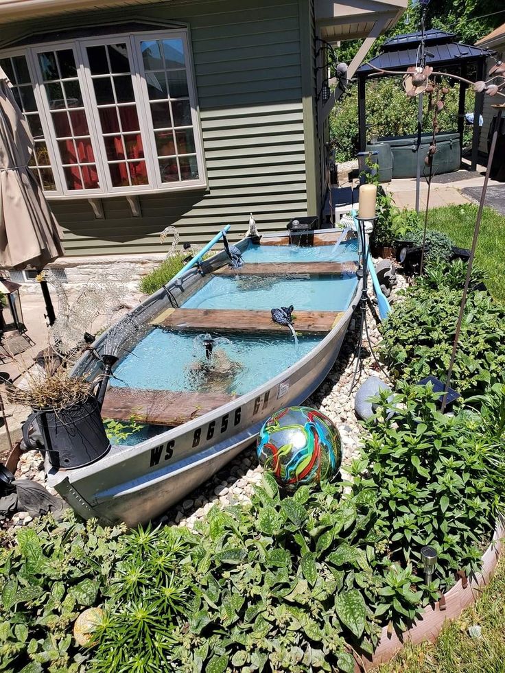 a boat sitting in the middle of a garden next to a house with plants growing around it