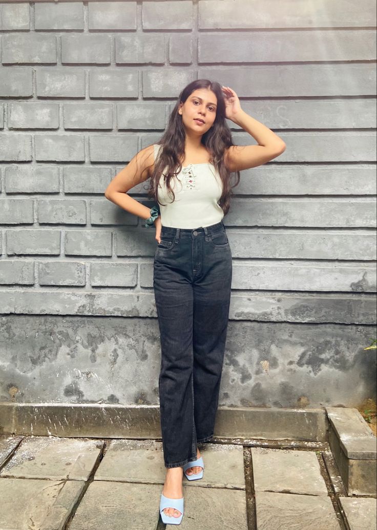 a woman standing in front of a brick wall with her hands on her head and arms behind her head