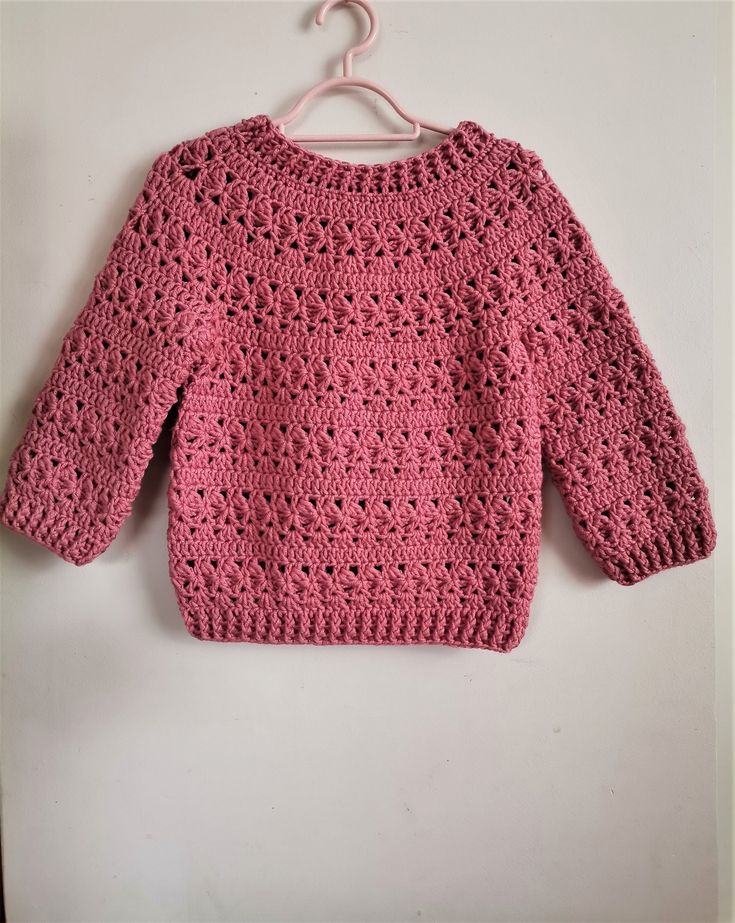 a pink crocheted sweater hanging on a white wall