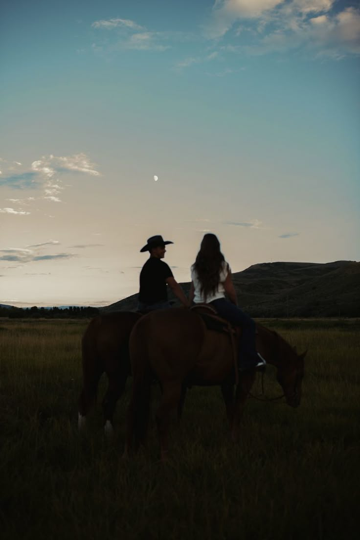 two people riding horses in a field at sunset