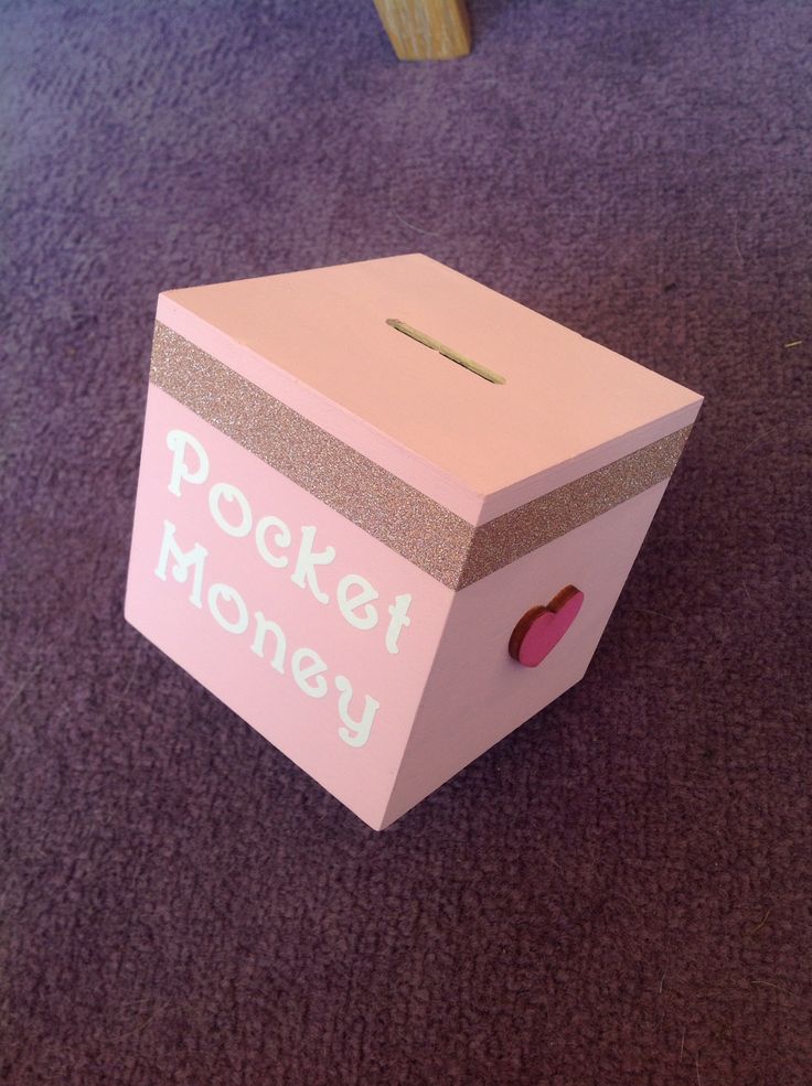 a pink box with the words pocket money on it sitting on purple carpet next to a wooden chair