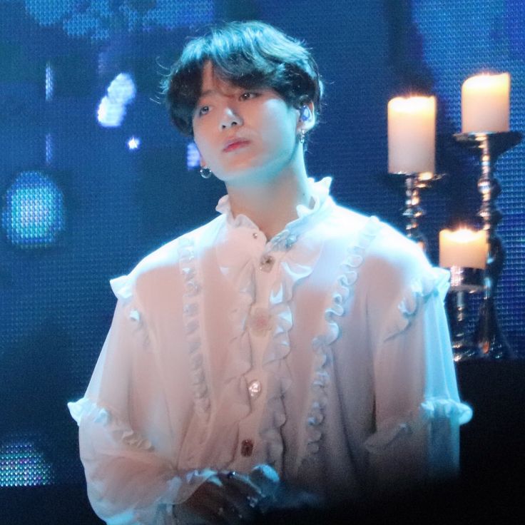 a young man standing in front of candles wearing a white shirt with ruffles on it