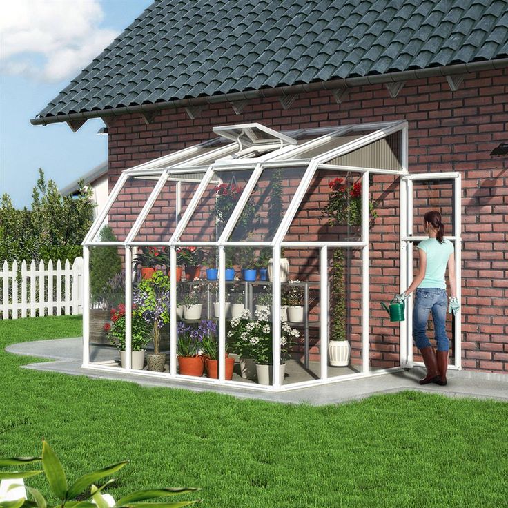 a woman standing in front of a brick building with a greenhouse on the lawn next to it