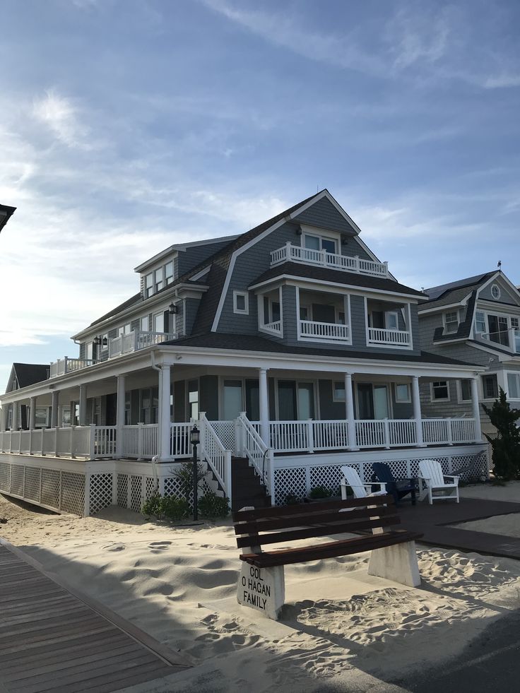 a large white house sitting on top of a sandy beach next to a wooden bench