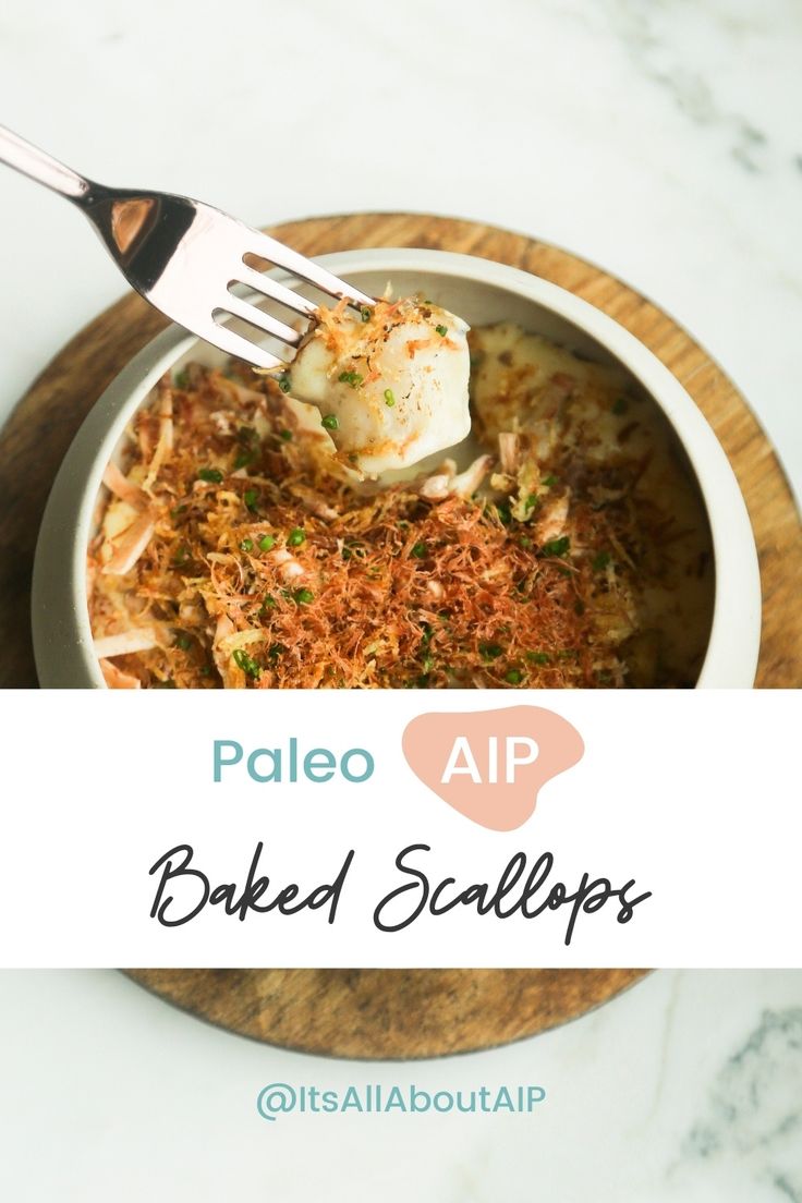 a bowl filled with baked scallops on top of a wooden cutting board next to a fork