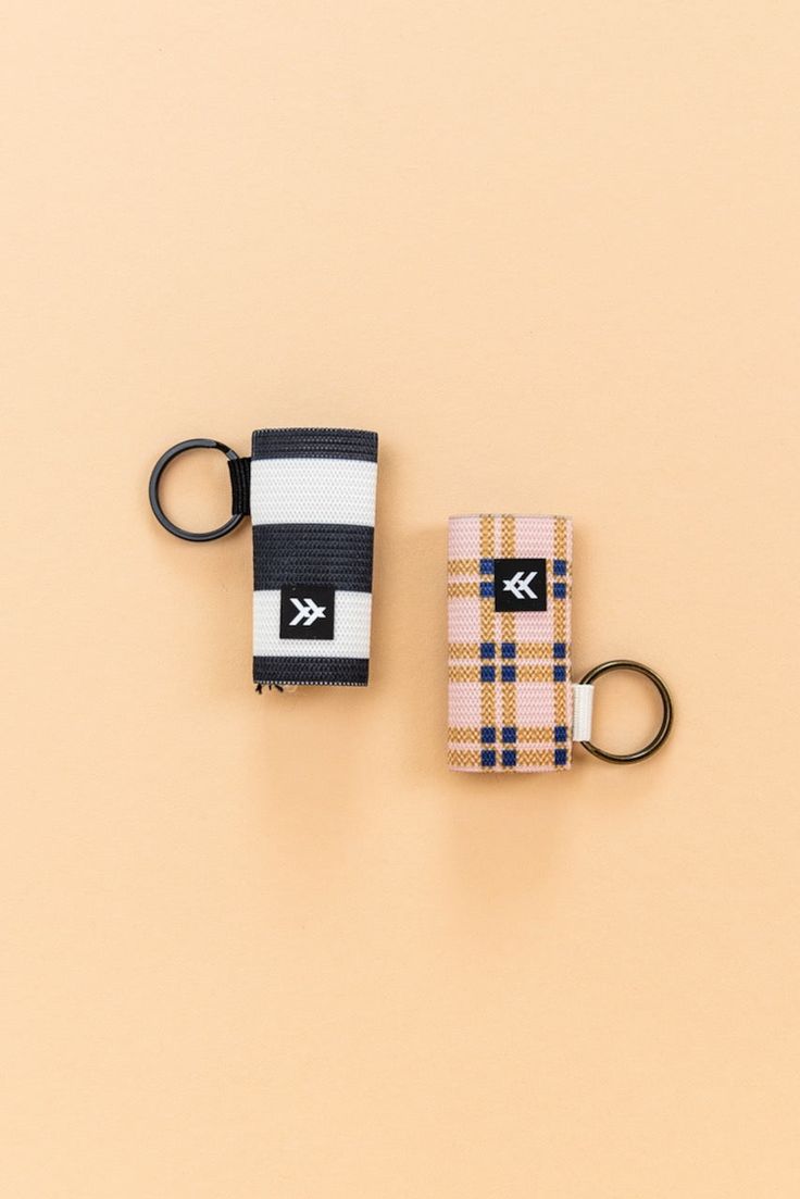 two keychains are sitting next to each other on a beige surface, one has a black and white stripe