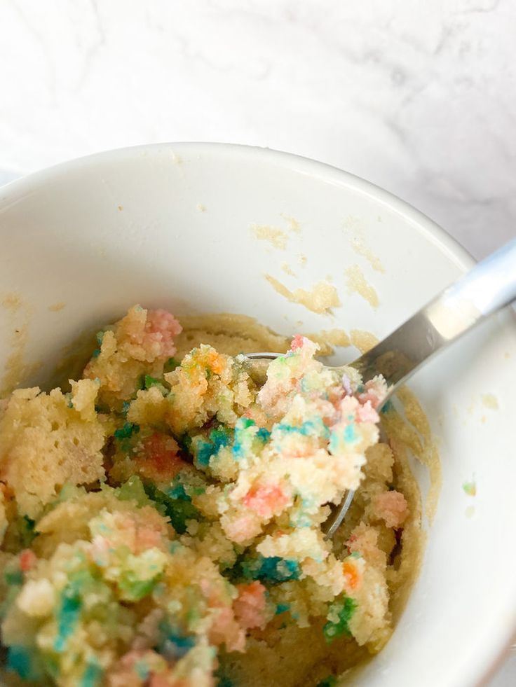 a white bowl filled with cake batter and sprinkles next to a spoon