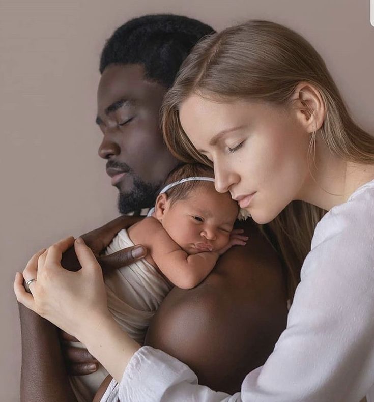 a woman holding a baby in her arms while standing next to a man with his eyes closed