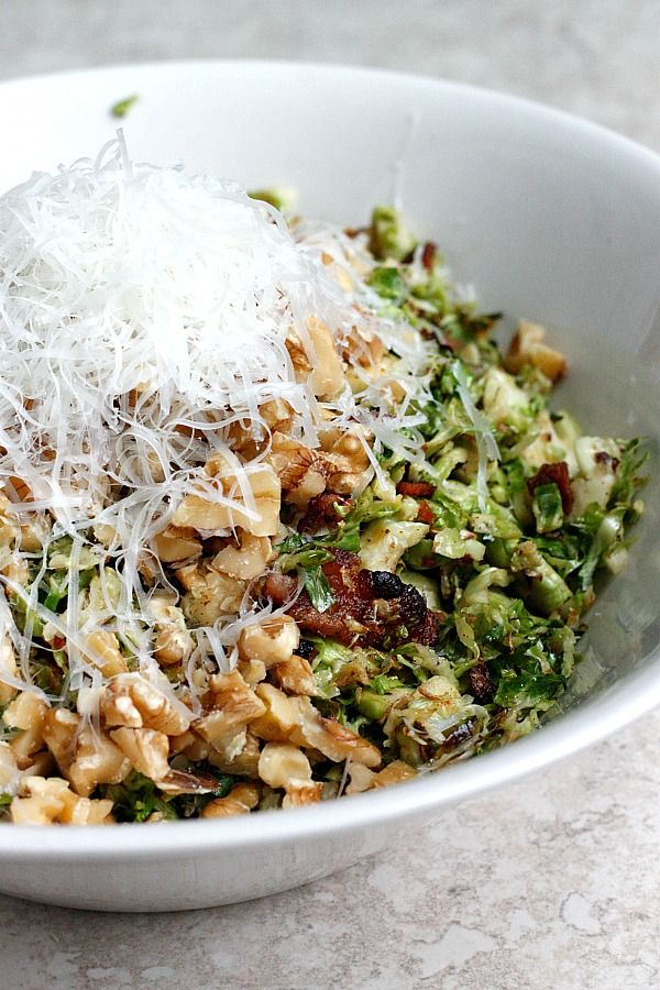 a white bowl filled with food and topped with parmesan cheese, nuts, and broccoli