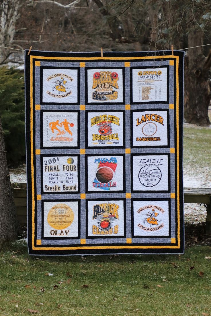 a quilt hanging from a clothes line on a tree in front of a park bench