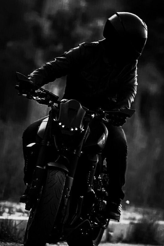 a man riding on the back of a motorcycle down a road in black and white