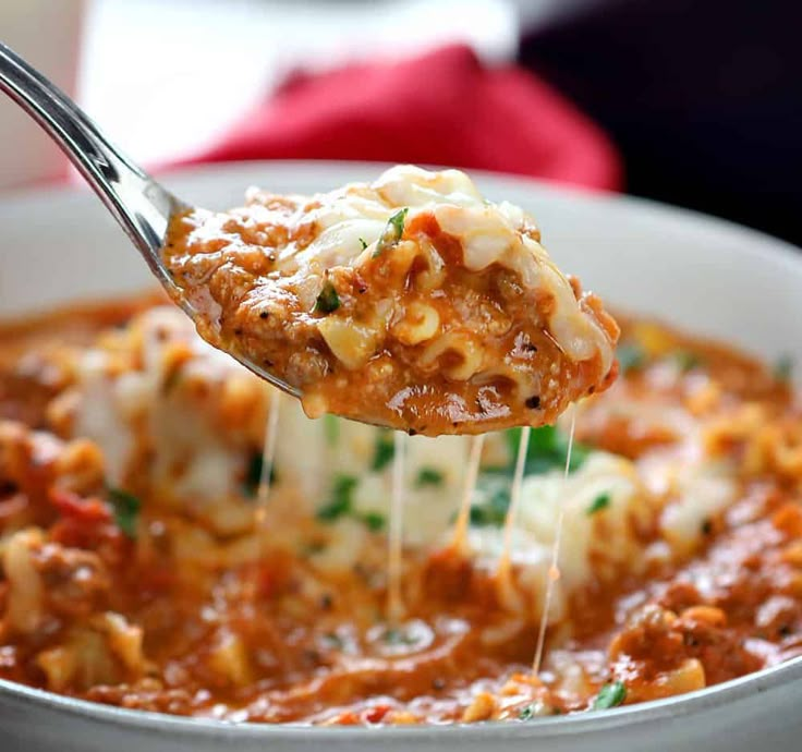 a spoon full of lasagna sauce being lifted from a bowl