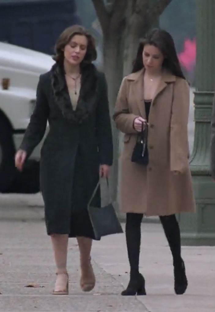 two women are walking down the street with their purses in hand and one is wearing a coat