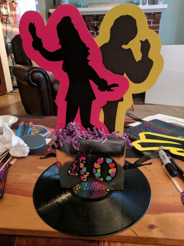 a birthday cake that is on top of a table with some paper cutouts in the shape of people