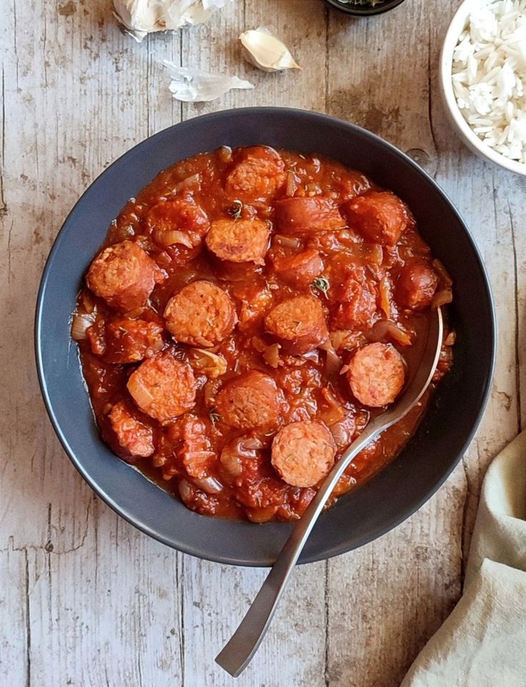 a bowl filled with meatballs and sauce on top of a wooden table next to rice