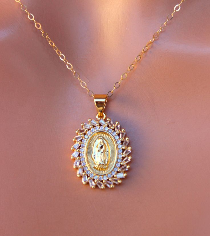 "This is a lovely 14kt gold filled Our Lady of Guadalupe pendant necklace. The absolutely stunning oval pendant measures 20x17mm, features Our Lady of Guadalupe image surrounded by sparkling crystals! Pendant comes on a 14kt gold filled shiny cable chain with spring clasp. Model is wearing a 16\" length, please choose your desired length. This is such a stunning pendant, even more impressive in person! Comes in a gift box, ready to present." Spiritual Oval Necklace Featuring Our Lady Of Guadalupe, Yellow Gold Oval Necklace With Our Lady Of Guadalupe, Spiritual Oval Our Lady Of Guadalupe Necklace, Yellow Gold Oval Jewelry With Our Lady Of Guadalupe, Oval Virgin Mary Jewelry Gift, Oval Yellow Gold Jewelry With Our Lady Of Guadalupe, Oval Our Lady Of Guadalupe Necklace For Gift, Oval Our Lady Of Guadalupe Necklace Gift, Oval Our Lady Of Guadalupe Jewelry Gift