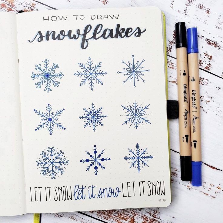 an open notebook with snowflakes drawn on it next to two markers and pens