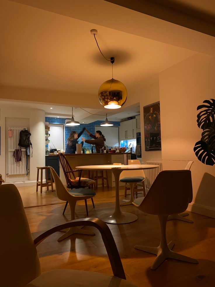 a living room filled with furniture next to a dining room table and two people in the kitchen