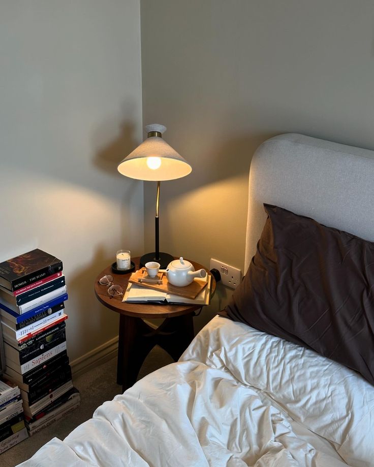 a bed with white sheets and pillows next to a night stand filled with books on it