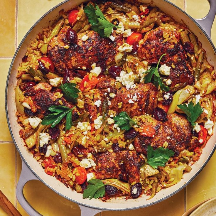 a skillet filled with meat and vegetables on top of a yellow tiled countertop