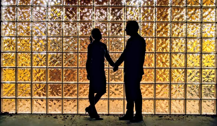 two people standing in front of a glass block wall with the light shining on them