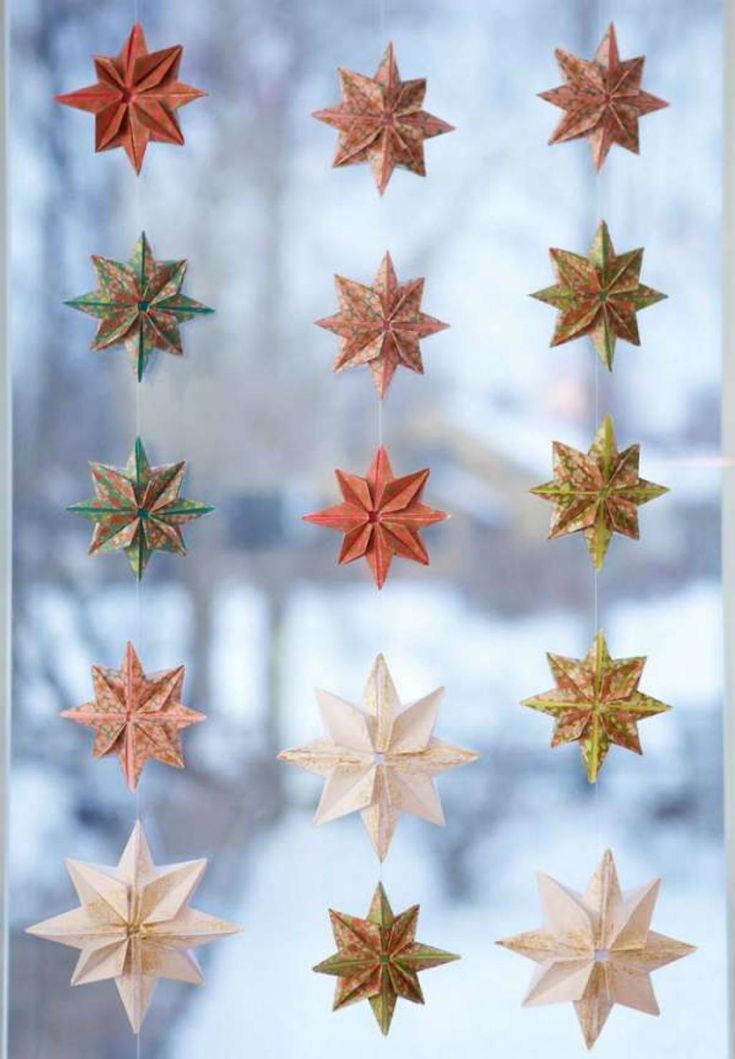 some paper stars hanging from a window sill in front of a snow covered tree