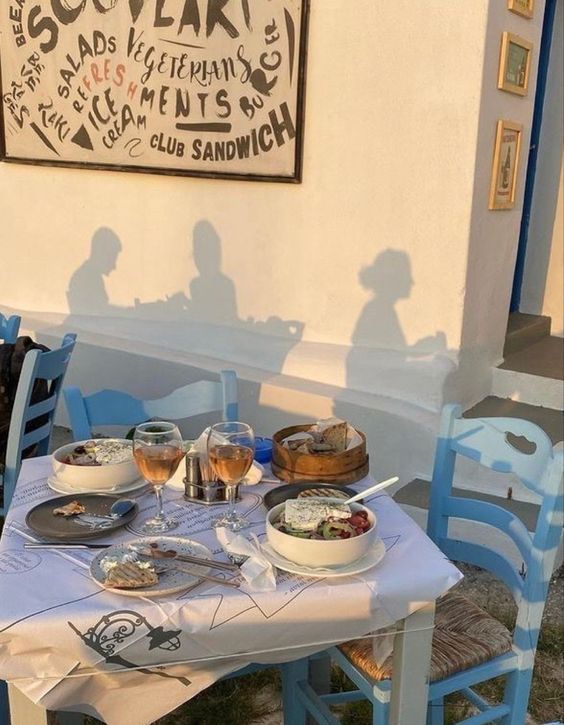 two people sitting at a table with food and drinks in front of a sign on the wall