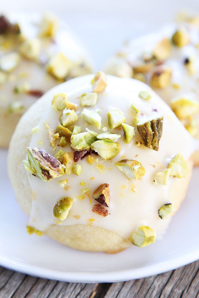 three cookies with white icing and nuts on a wooden table, one has pistachios sprinkled all over it