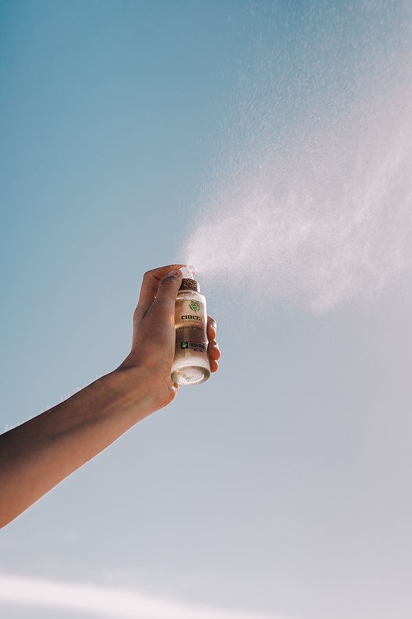 a person holding a spray bottle in their hand and spraying it with the sky behind them