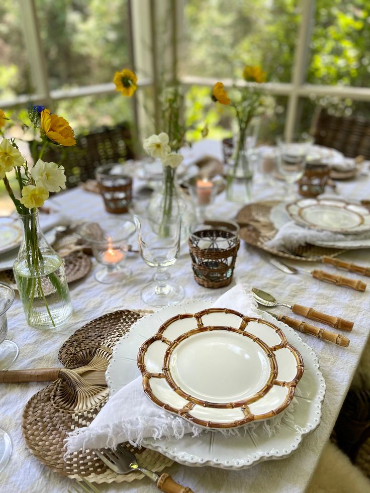 the table is set with plates, silverware and flowers in vases on it