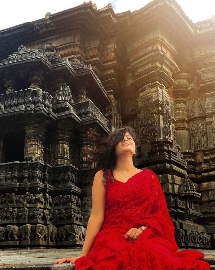 a woman in a red dress is sitting on the steps outside an ornately carved building