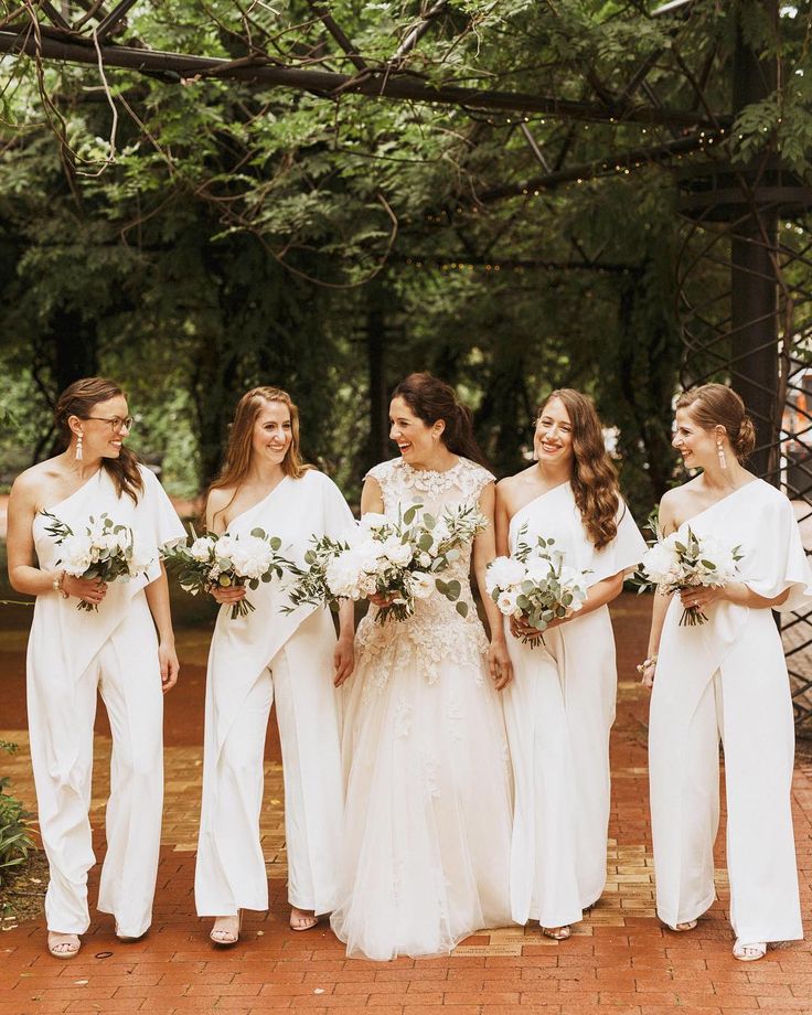 a group of women standing next to each other wearing white dresses and holding bouquets