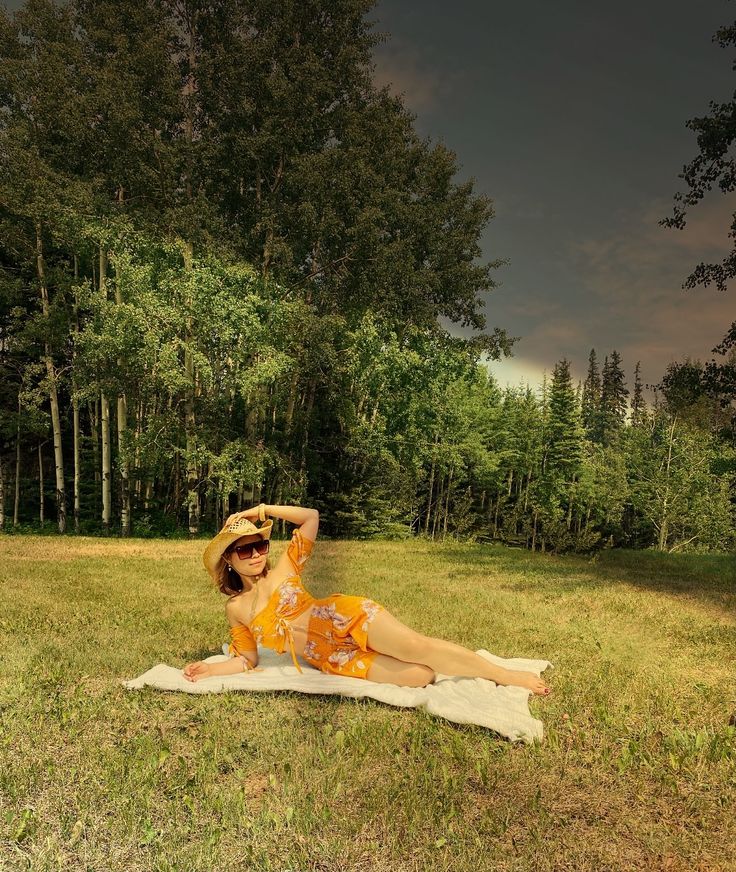 a woman laying on top of a towel in the grass next to some trees and bushes