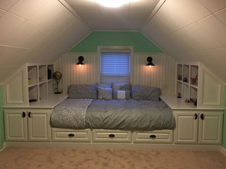 a bed sitting in the middle of a bedroom under a slanted ceiling with built - in bookshelves