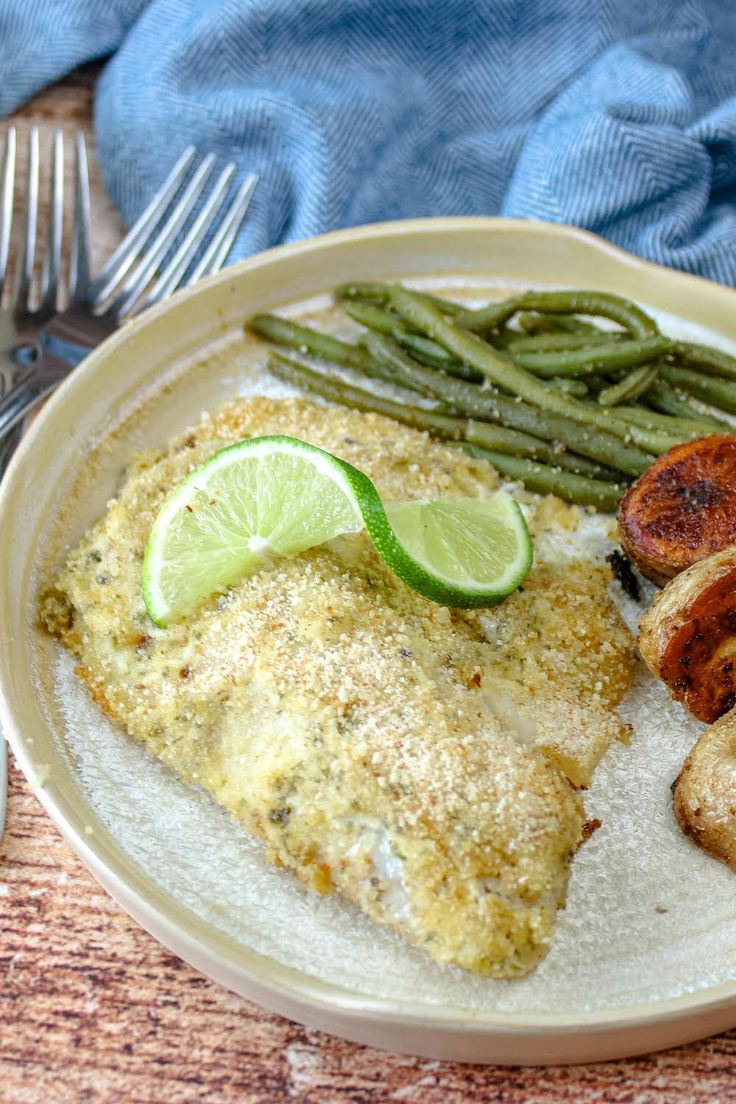 a white plate topped with fish, green beans and potatoes next to a slice of lime