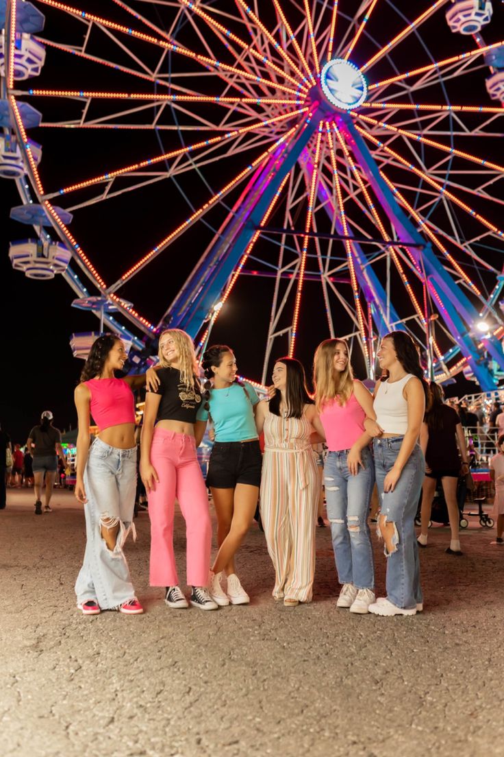 four girls standing in front of a ferris wheel at night