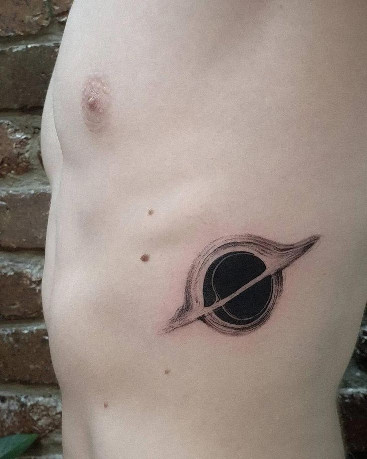 a small saturn tattoo on the side of a man's stomach, with an arrow in it