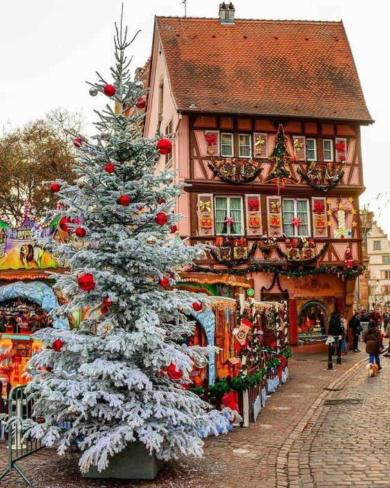 a christmas tree in front of a building with decorations on it and people walking around