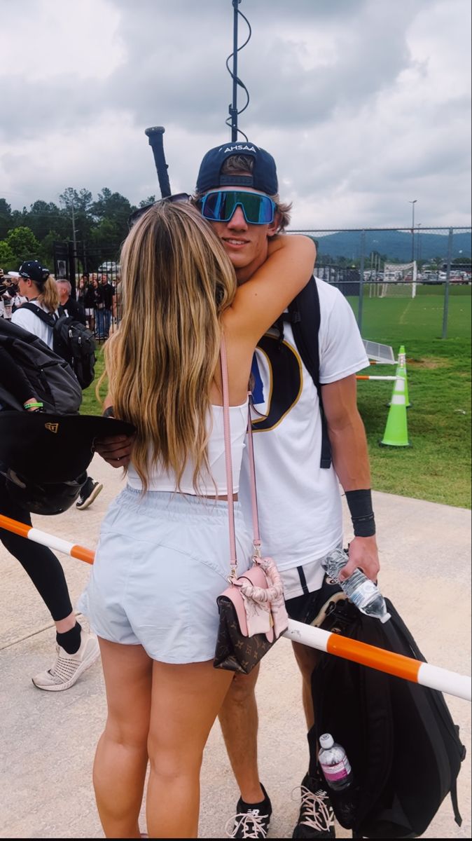 a man and woman hugging each other in front of a baseball field