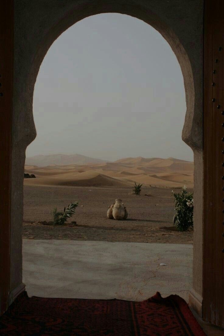 an arch in the middle of a desert with a camel laying on it's side